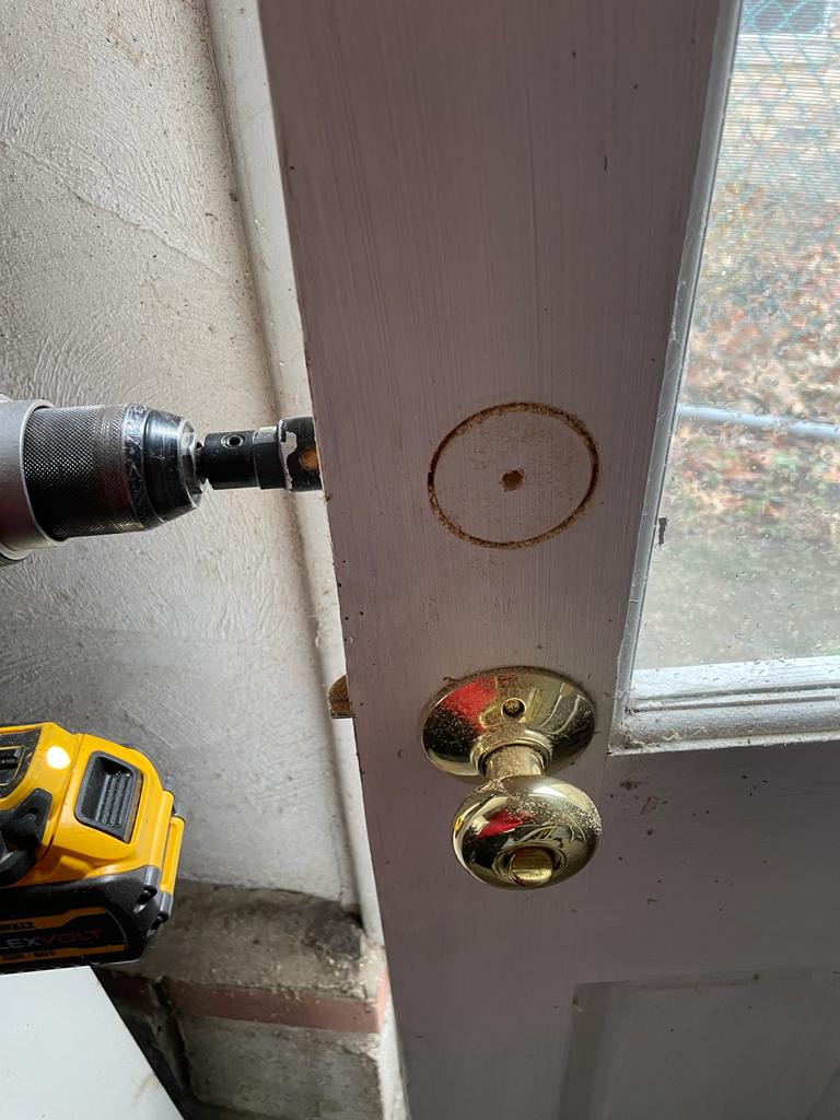 A locksmith is adding a new lockset to wood door (4)